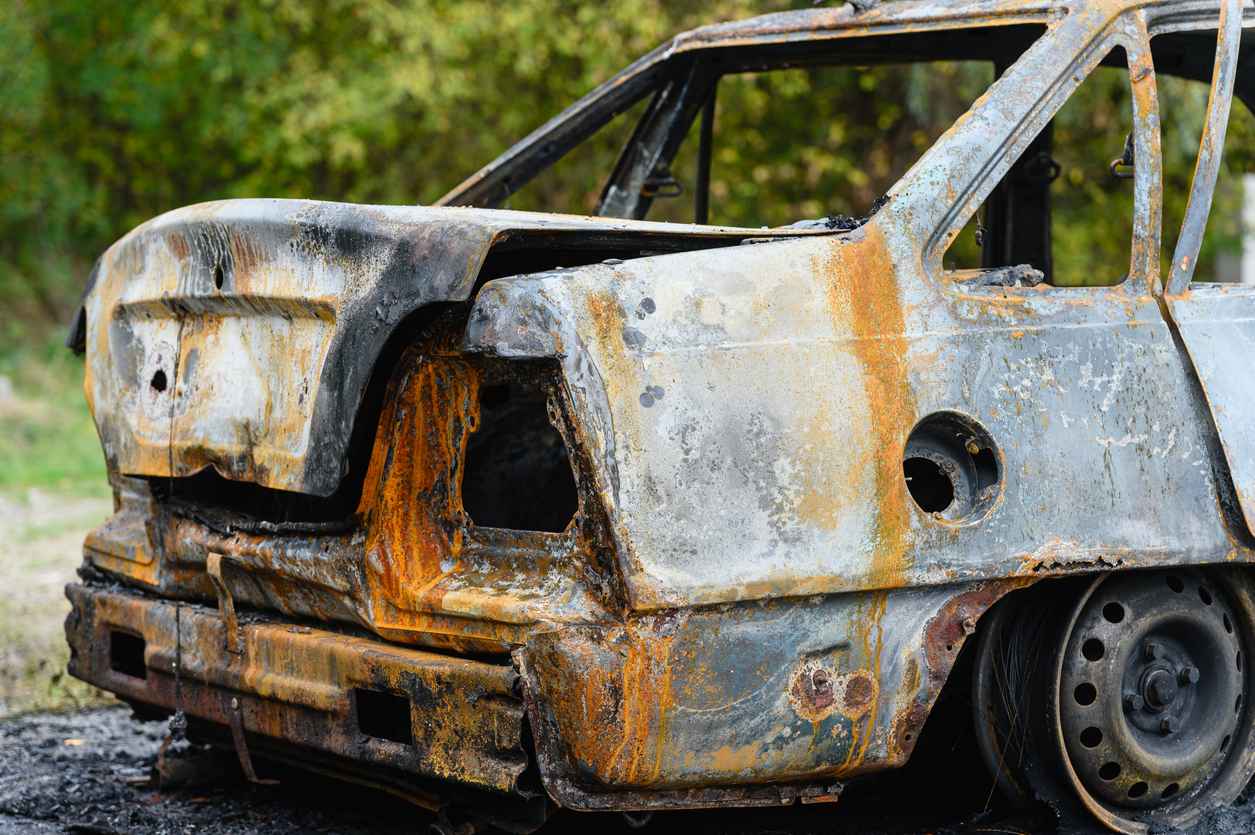 Burned car wreck abandoned on roadside in nature. Close-up of the trunk of a burnt-out car.